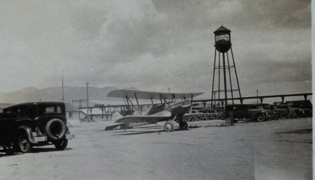 Black-and-white photograph of the Alexander Industries plant at Colorado Springs, with biplanes on the field and a water tower.